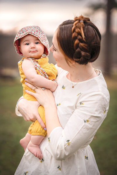 A mom with braids in her hair is holding her young baby while her baby is smiling at the camera.
