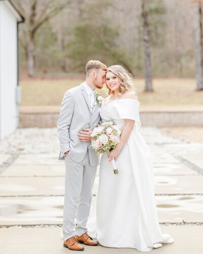 A Little Rock Wedding photography image of a bride dressed in long white gown and groom in his light gray suit snuggle on a patio at sunset