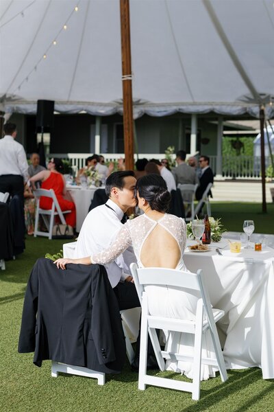 A wedding couple sitting together and leaning in for a kiss 