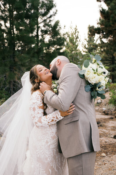 Romantic coastal wedding photo of couple sitting on seaside rocks laughing together
