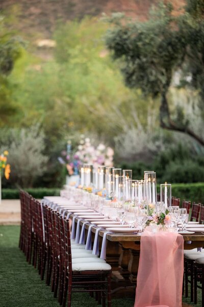 Large reception table set with candles, florals, and dinner wear with the trees and greenery around it.