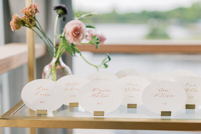 Oval cream escort cards with calligraphy on gold shelf for Mystic, Connecticut wedding.