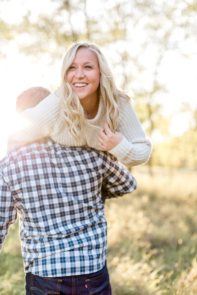 Man carries fiancee on his shoulder through a MInnesota field during engagement photo session.
