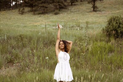 woman wearing a white dress standing in a field with her eyes closed and her arm up