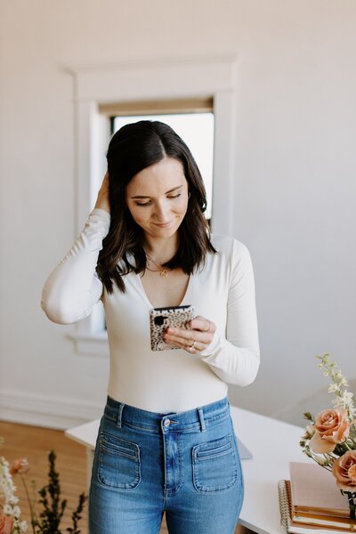 woman with white shirt and jeans on her phone
