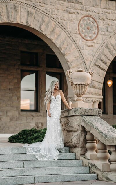 MODERN MIXED-FABRIC WEDDING GOWN WITH HIGH HALTER NECKLINE This sultry and stylish silhouette from Miss Stella York is perfect for an adventurous wedding day statement. Lace over crepe gives a softer, lighter feel that is both easy to wear and effortlessly sexy—making it the perfect accompaniment to a beach or garden wedding. A high neckline with skinny center plunge offers a hint of modern sexiness, while light beadwork offers the touch of decadence you crave. Curved seaming and graphic laces are thoughtfully placed along the figure to flatter the curves for a universally flattering silhouette, while a long lace inset feature in the middle of the train widens toward the hem for a stunning hourglass effect. Floating laces and an X-back feature top the look with simple yet stunning detail, keeping all eyes on you ask you walk toward wedded bliss.