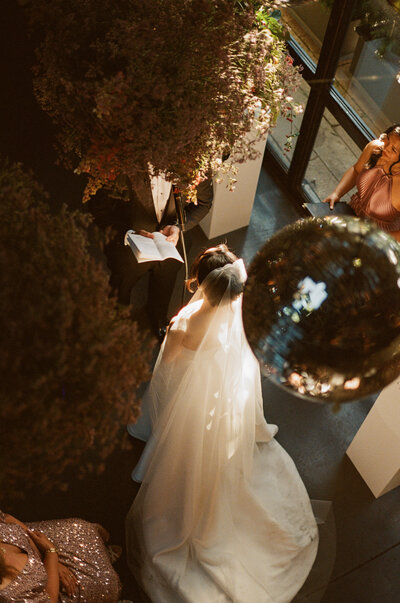 A waiter elegantly pours red wine into a glass, captured on film with soft, moody lighting during a wedding reception