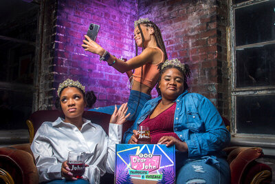 3 black women wearing tiaras holding wine glasses and cell phone branding photo
