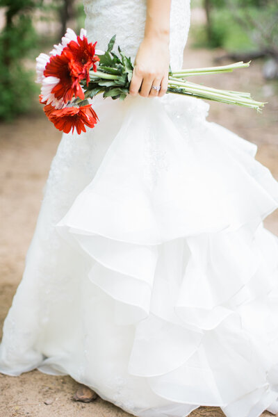 Bride holding red flowers while wearing white wedding dress