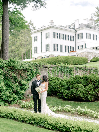 Bride and groom stand in the garden with The Mount, Edith Wharton's Home in the background