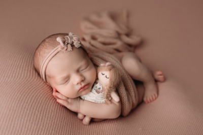 Newborn baby girl is peacefully posed, wrapped in soft pink fabric, radiating warmth and sweetness. Her delicate features and serene expression are highlighted against the cozy, neutral-toned backdrop at Paula Goforth Studio, located in Fort Worth, creating a timeless and tender portrait.







