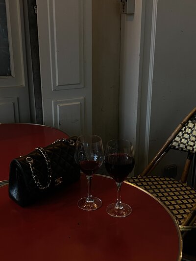 Two glasses of red wine and a designer handbag on a Parisian cafe table