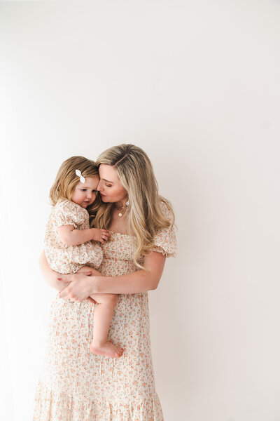Mom with daughter in matching floral dresses.  Mom kissing daughter on the head,taken by Stickan Photography as an Andover Newborn Photographer