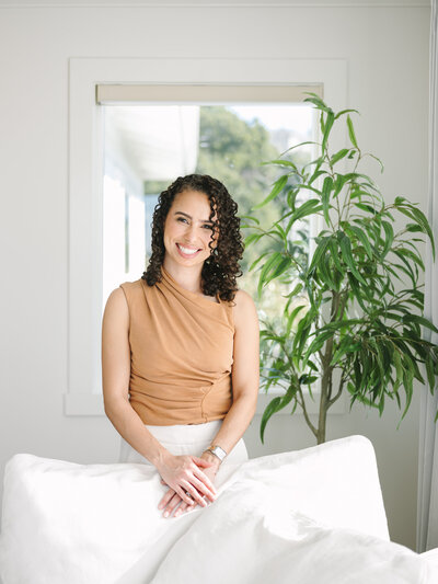 Woman standing in front of a white couch and green plant during her brand session with Krista Marie