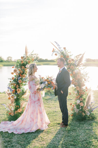 Bride and groom getting married in front of water and a floral backdrop