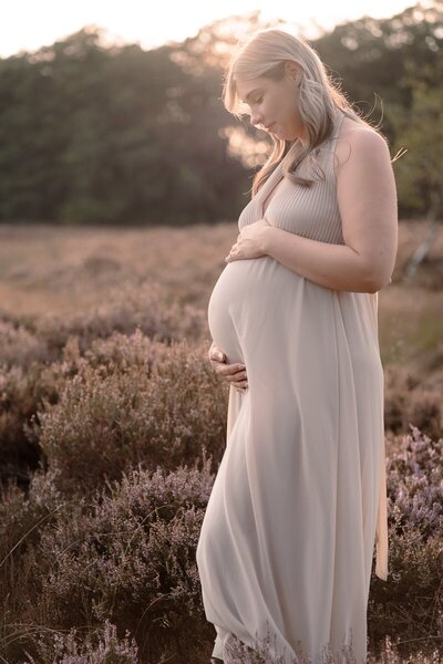 zwangere vrouw heeft haar handen op haar buik en kijkt liefdevol naar haar buik tijdens een zwangerschapsshoot.
