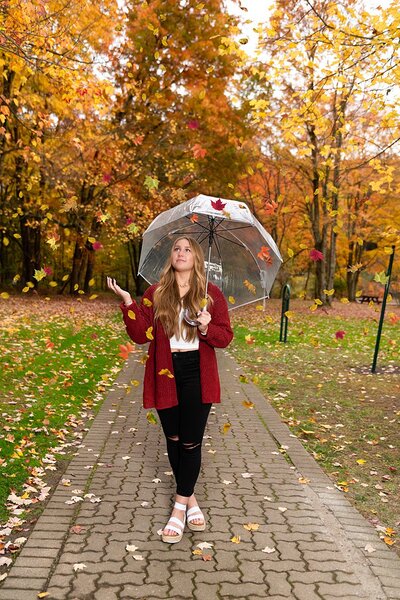 High school senior girl holding an umbrella and looking up as fall leaves fall around her