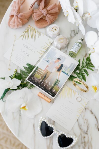 Save the dates, wedding invitations, jewelry, rings, and shoes laid out on a table 
