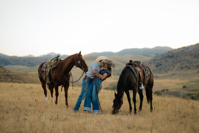 man and woman embracing in a field with their horses in wyoming
