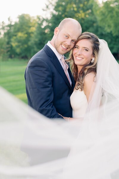 bride and groom smiling while the bride's veil flows in the wind