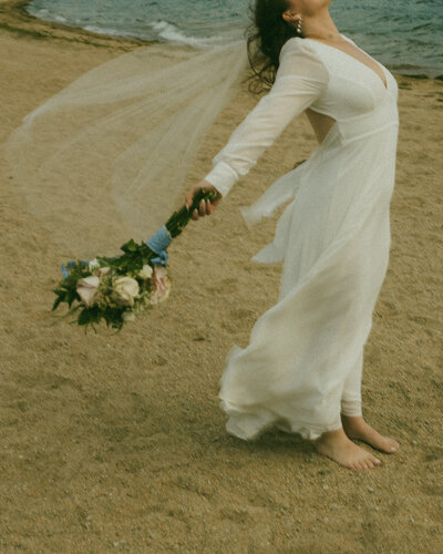 bride holding flowers on beach dress and veil blowing in wind