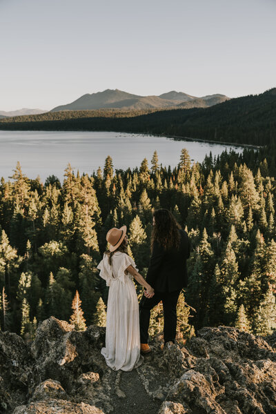 Bride and groom holding hands standing on a rock overlooking forest and Lake Tahoe by Lake Tahoe elopement photographer Kasey Mantiply