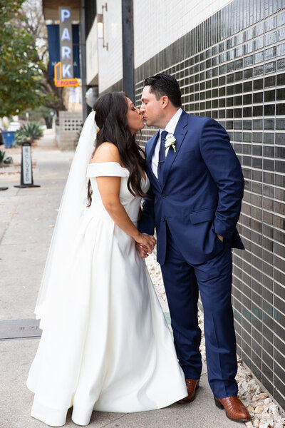 An Austin-based wedding photographer captures a heartwarming moment of a bride and groom kissing in front of a building.