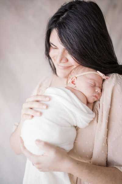 Newborn Portrait taken in a studio in Jacksonville with the mother in a blush dress while the baby sleeps on her shoulder in an ivory swaddle