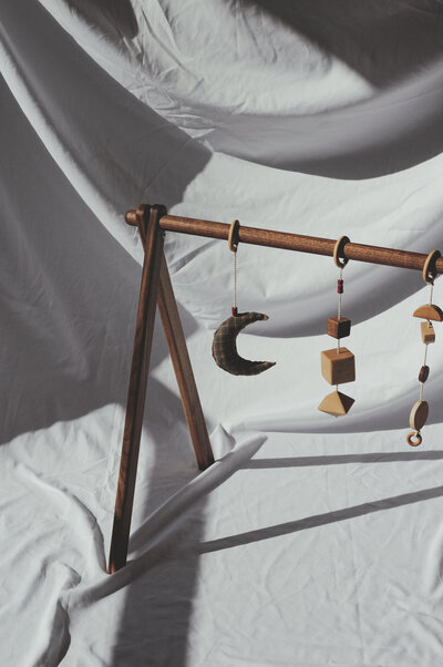 A solid walnut baby gym made with wood and cotton montessori inspired toys made sealed with a non toxic wax