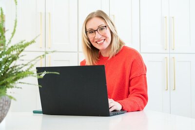 A woman wearing glasses smiles while working on her laptop, symbolizing a therapist in Ontario, Canada.