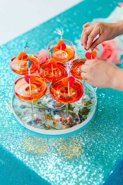 A person adding a garnish to a cocktail glass on a tray with other drinks.