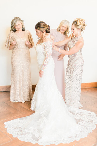 bridesmaids and mom in cream colored dresses helping a bride get into her dress at black canyon inn wedding venue taken by colorado wedding photographer kari joy