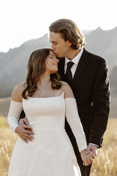 groom and bride embrace with rocky mountains in the background.