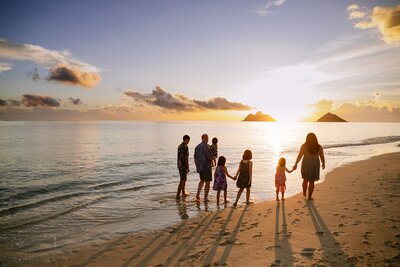 A family of seven walk along the beach at sunset.