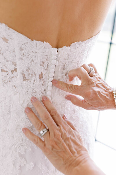 Hands do up the buttons that line the back of bride's wedding gown