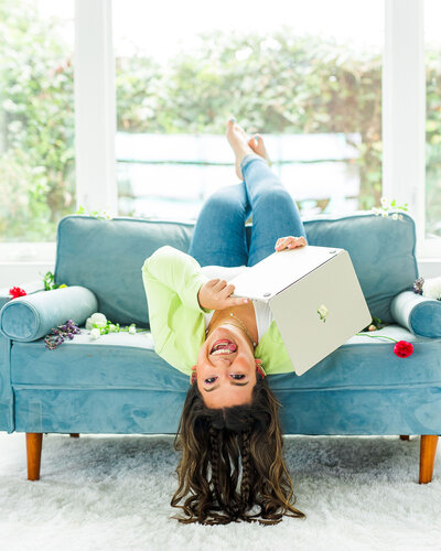 Makayla Rivera laying upside down on a blue chair holding a laptop