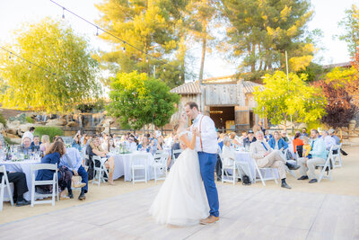 Bride and groom have their first dance at their outdoor wedding reception with guests watching and green trees in the background. Photo by sacramento wedding photographer, philippe studio pro.