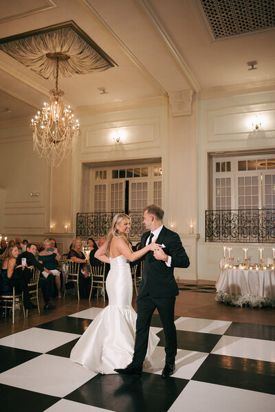 A bride and a groom are dancing in Philadelphia Pennsylvania on top of a black and white checkered floor smiling. 