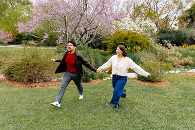 Couple walking hand-in-hand through lush greenery during their engagement session at the LA Arboretum