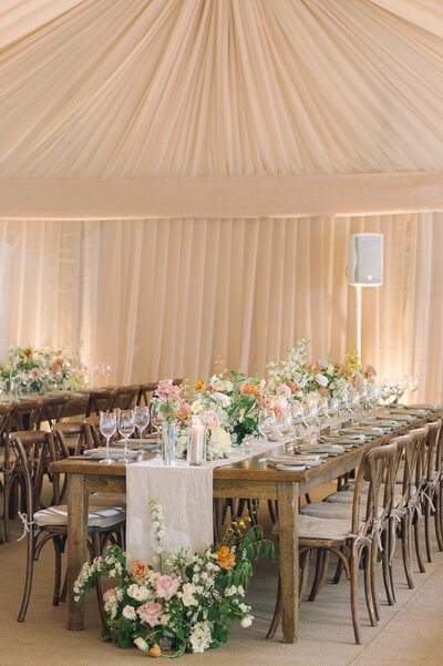 Wedding reception in a blush coloured tent with wodden tables covered in pink and cream flowrs