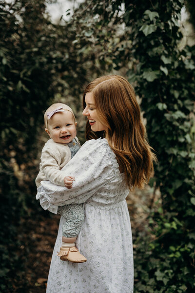 mother holding baby in front of a hedge