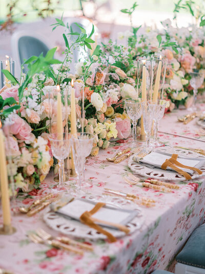 Luxury event long dining table with pink patterned linen and pink and yellow spring flowers in the middle