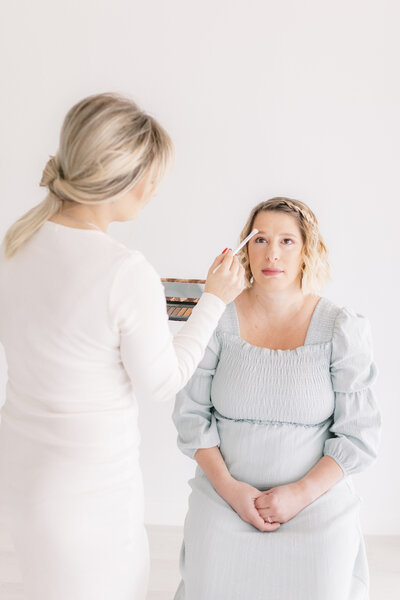 Newborn client mother getting her hair and makeup professionally done in white studio