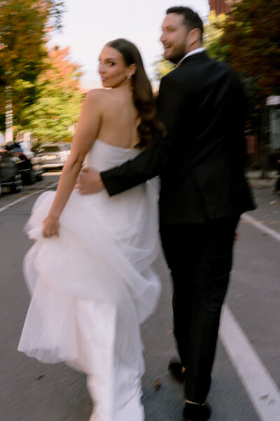 blurry picture of bride and groom walking down a street as they both look over their shoulders
