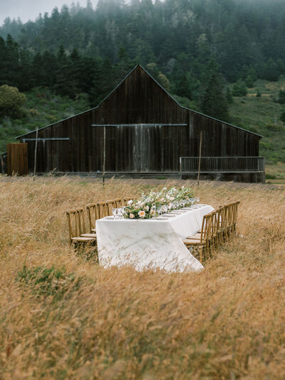 a table full of flowers with a brown barn behind in a field by colorado wedding photographer JKG photography