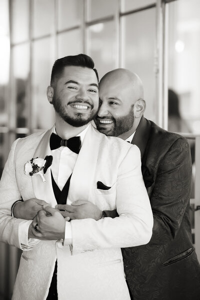 A person standing behind their partner with their arms around them on their wedding day 