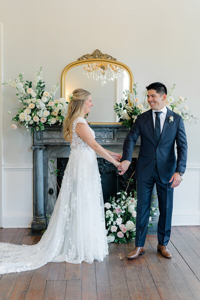 couple naturally enjoying moment together at gadsen house standing in front of fireplace, gold mirror and florals