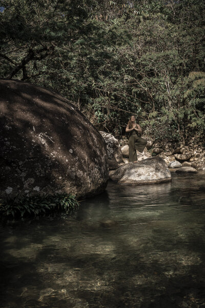 Una mujer hace meditación en la selva con un río