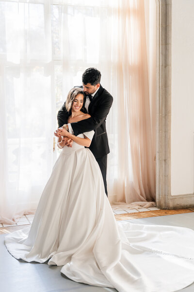A bride and groom at Callanwolde Fine Arts Center in Atlanta embracing eachother in a hug, while the groom kisses his bride on the top of the head.