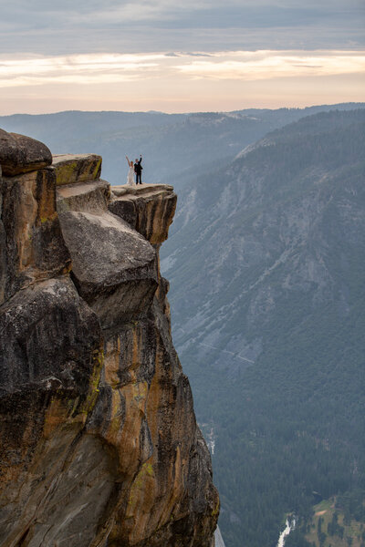 A newlywed couple celebrates on the edge of Taft Point during their Yosemite elopement, with sweeping mountain views behind them. Captured by Yosemite elopement photographers, this adventurous moment showcases the thrill of saying 'I do' in nature.